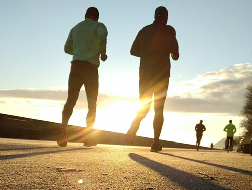 The back of two runners jogging towards the sun on a path