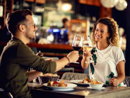 Two people raising a glass of wine at a restaurant table with food on