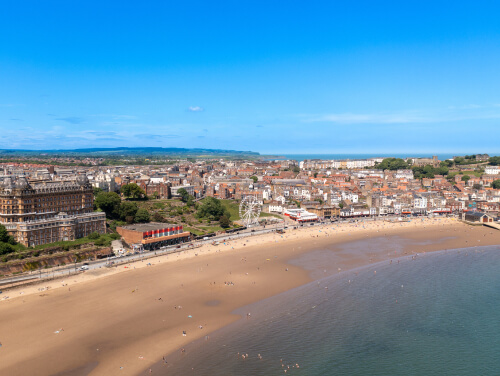 A beach with lots of people on it, you can see a town centre behind the beach.